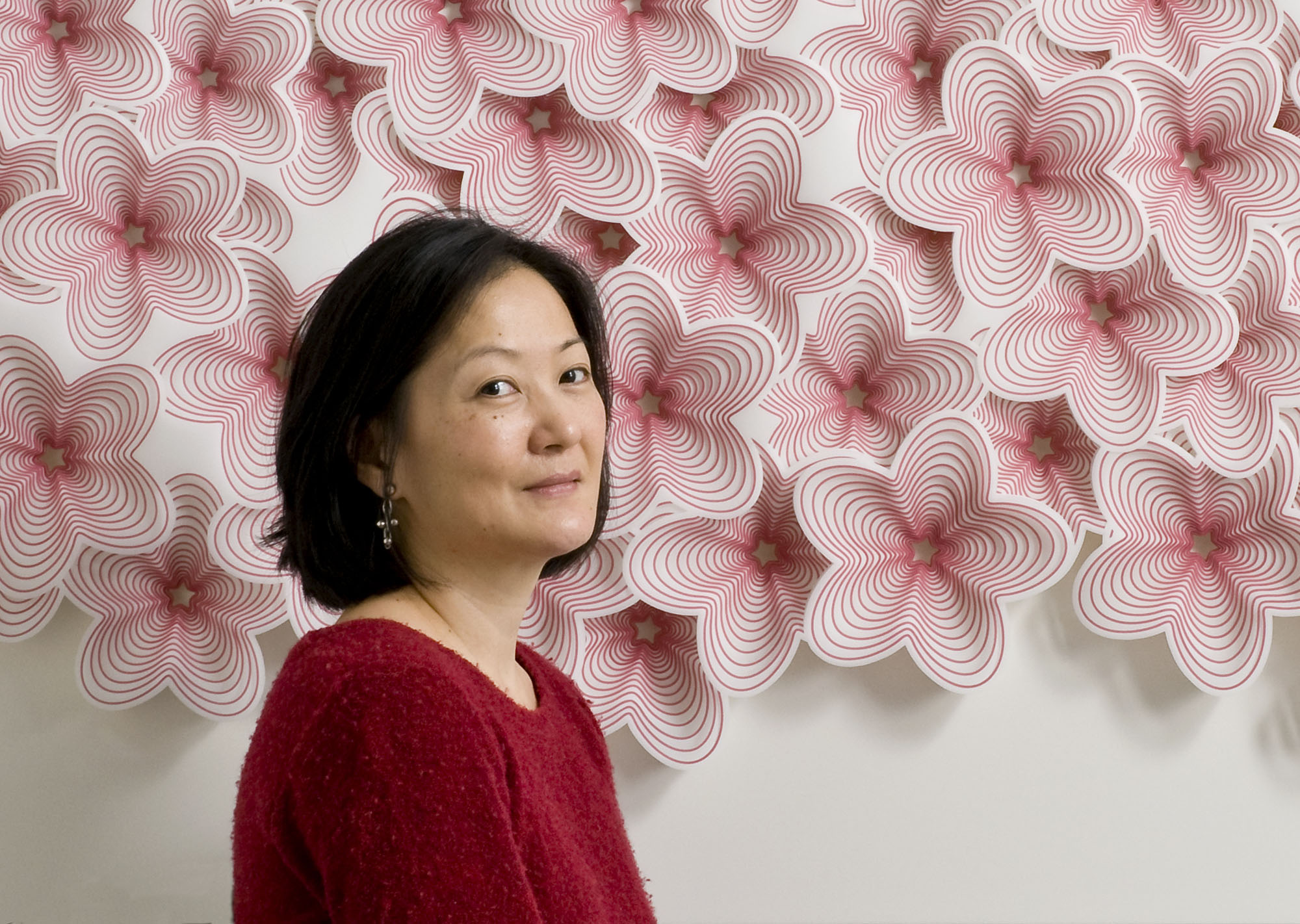 Photo of artist Imi Hwangbo in front of colorful pink and white flower cut art