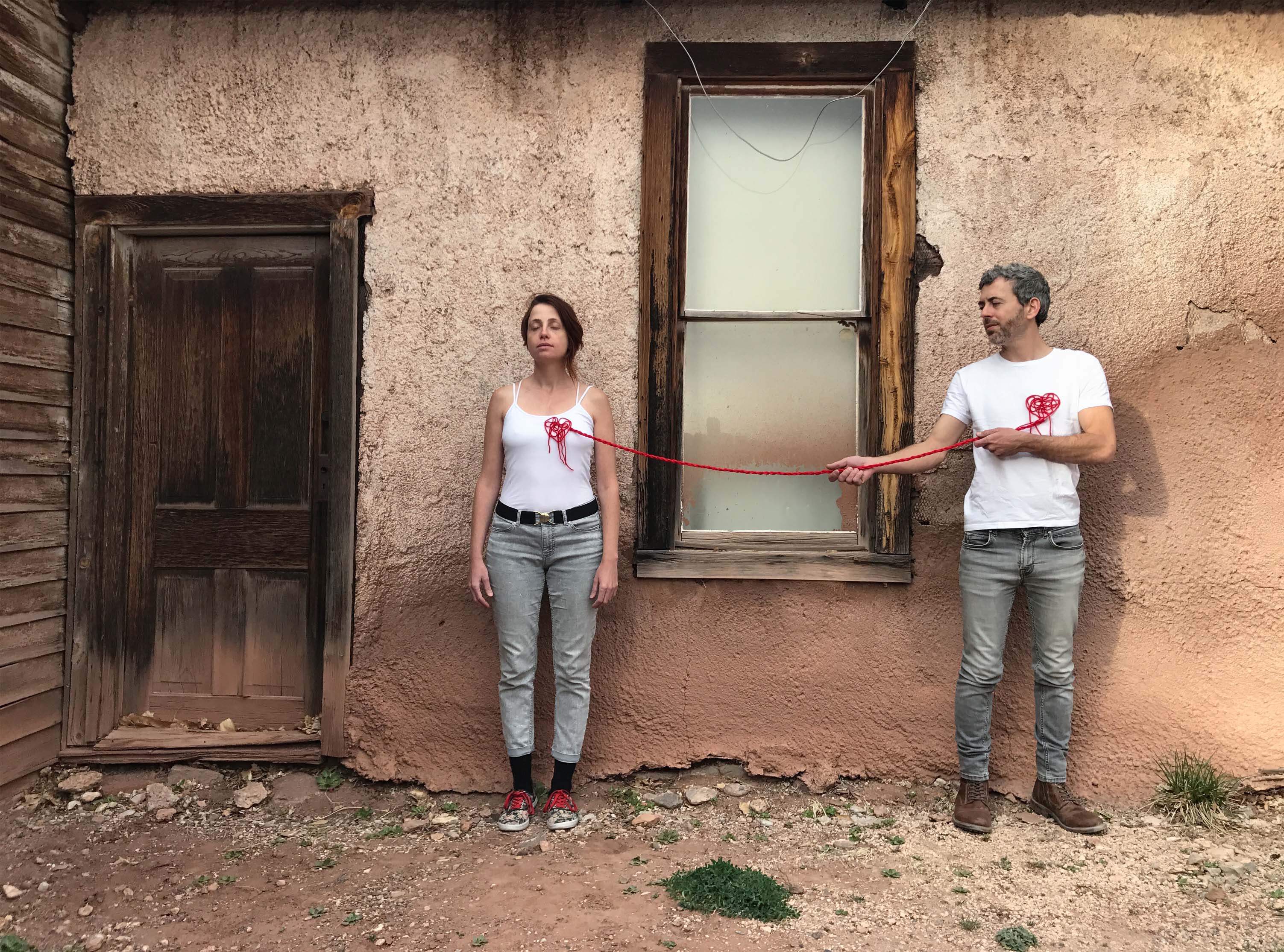 artists Maya and Roie standing in front of wall with red string connecting them