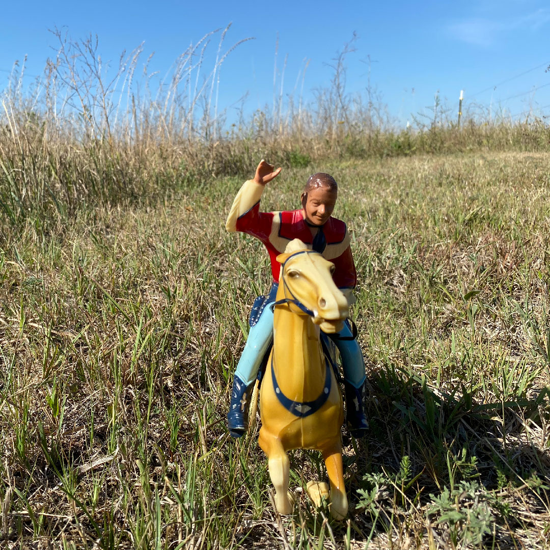 little plastic cowboy riding a little plastic horse in a meadow