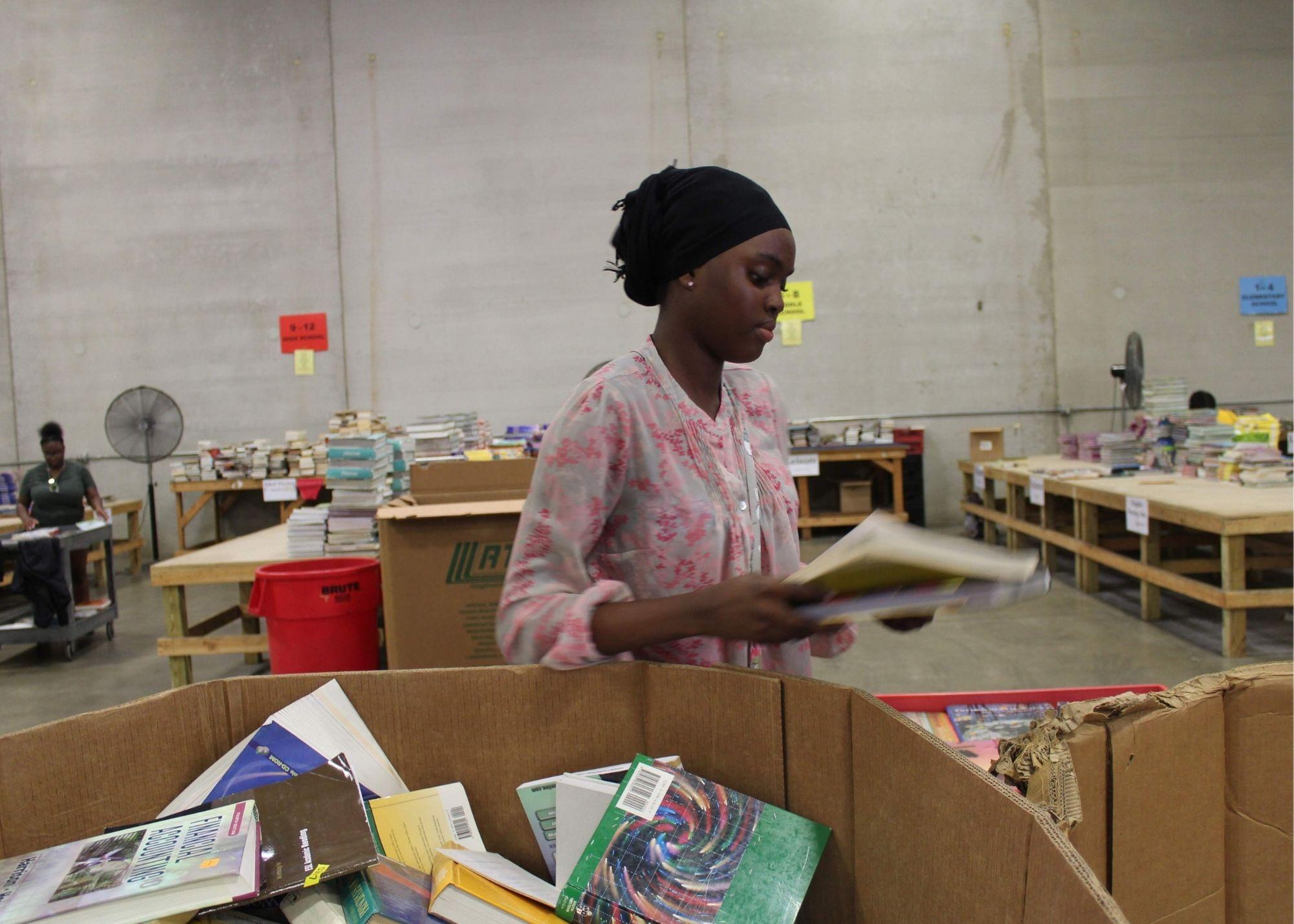 A woman at a book drive event holding books. / KSU TRiO students give back to the community through a book drive event.