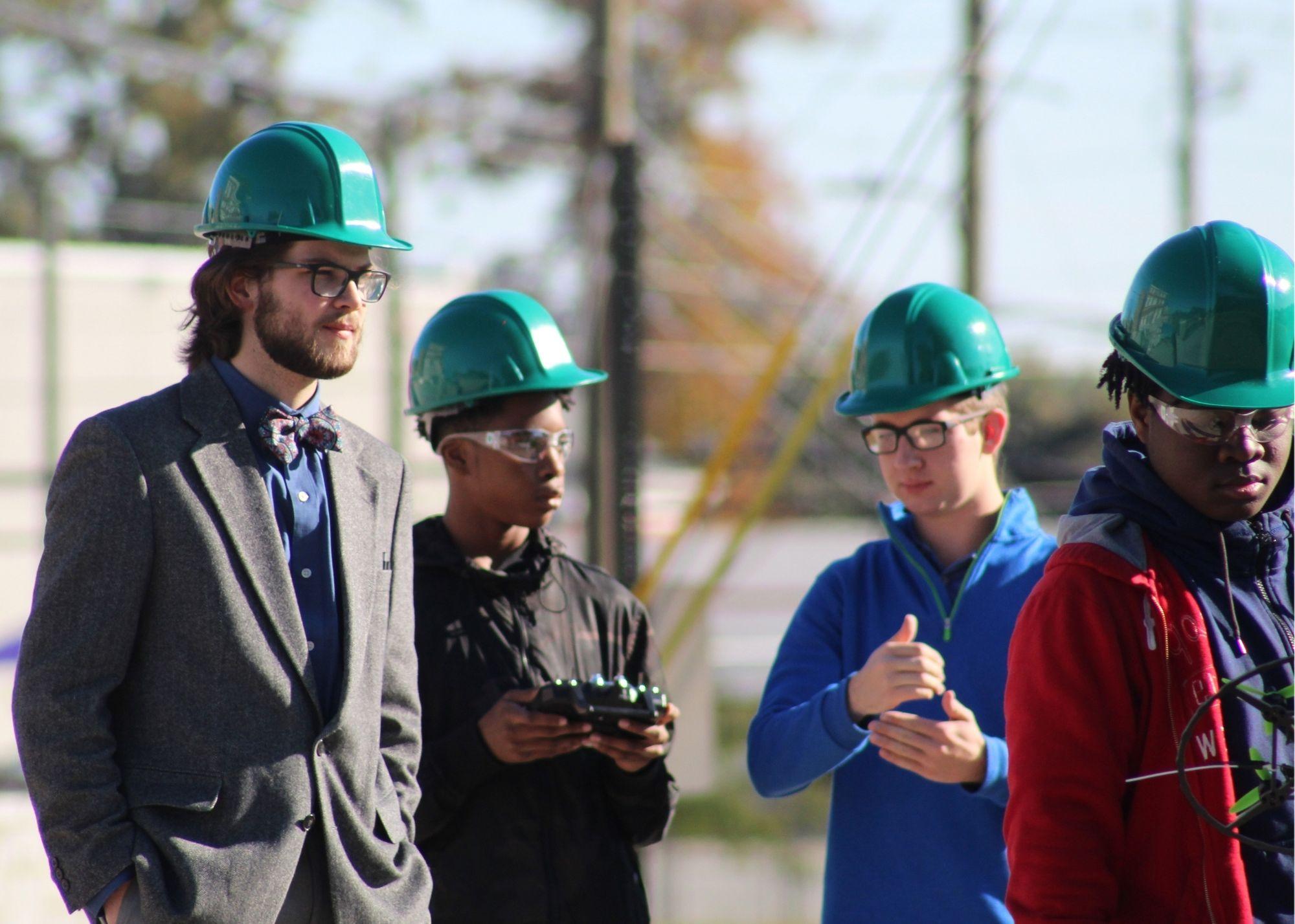 Four students wearing hardhats, with one holding a remote control and another holding a drone. / KSU TRIO's groundbreaking Drone Program introduces students to the basics of drone flying, ethics, and mechanics, and the program gives students the opportunity to test for their FAA Pilot's License