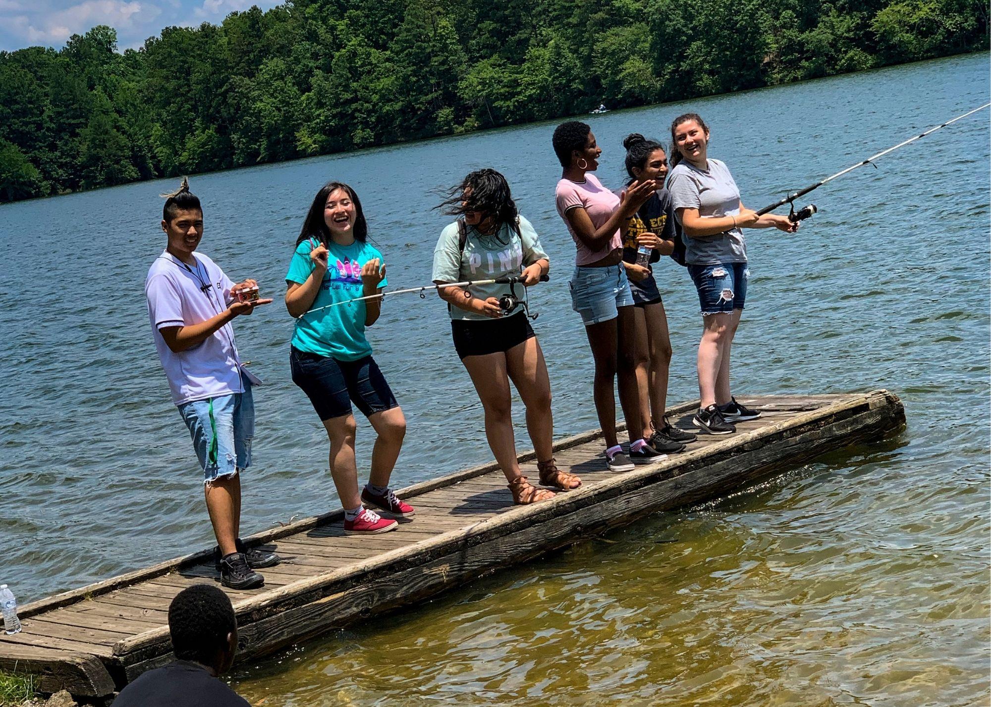 Students standing on a wooden pier, holding fishing rods and fishing. / Hiram High School Upward Bound learns about ecological preservation.