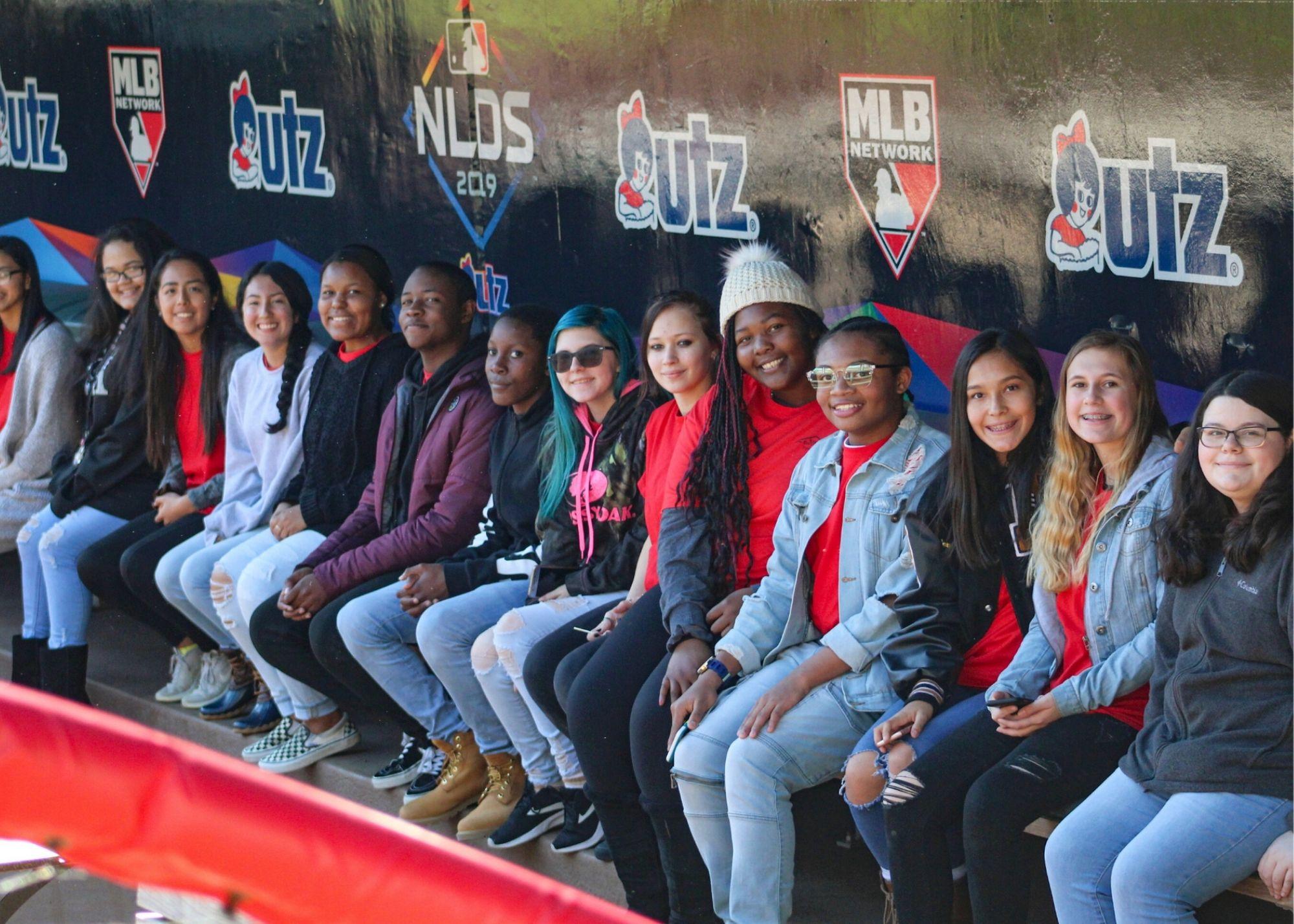 Students smiling and sitting in front of a wall painted with the MLB logo and UTZ logo. / KSU TRiO Upward Bound at Rockmart and Cedartown High Schools visit the Suntrust Park to learn about stadium construction and architecture.
