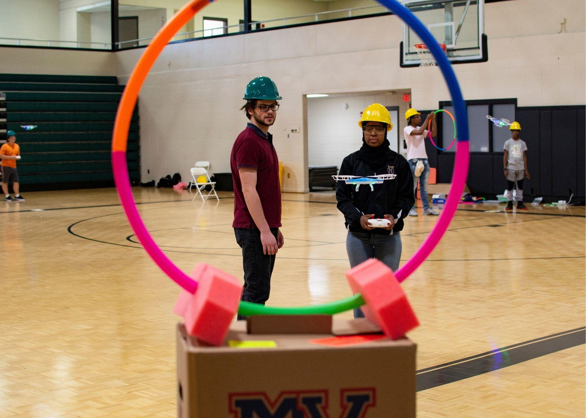 Students in a gym setting wearing hardhats and flying drones / KSU TRIO's groundbreaking Drone Program introduces students to the basics of drone flying, ethics, and mechanics, and the program gives students the opportunity to test for their FAA Pilot's License