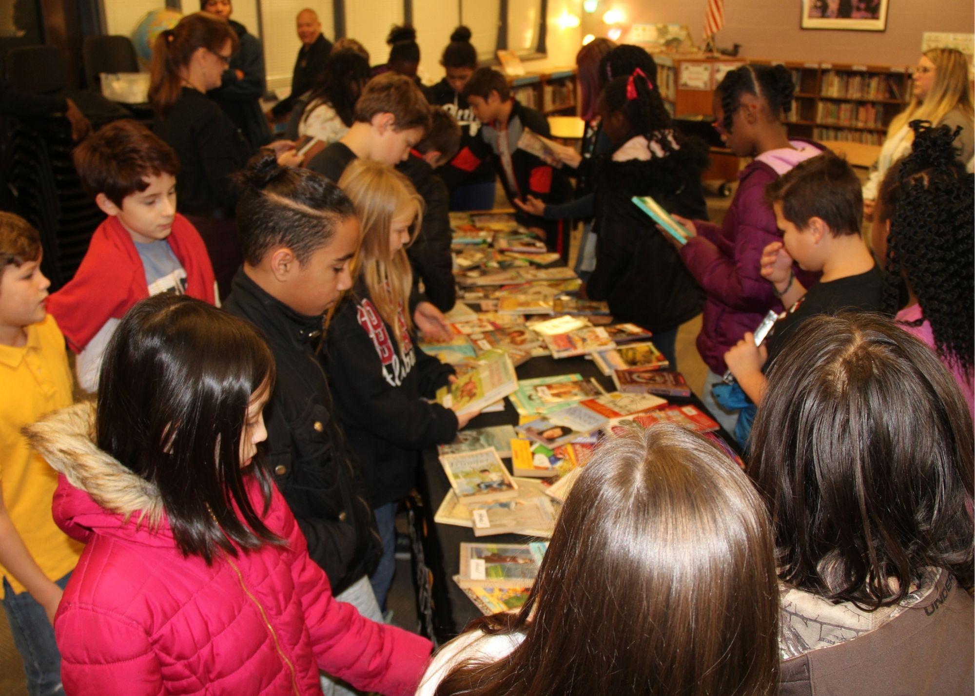 Young students attending a book drive, looking at books on a table. / Students and staff from the Kennesaw State University and the Georgia Highlands College Paulding Site provided a special Book Drive for Villa Rica students. The groups went to Villa Rica Elementary School with hundreds of free books in order to give students access to a variety of reading material to build their reading skills.