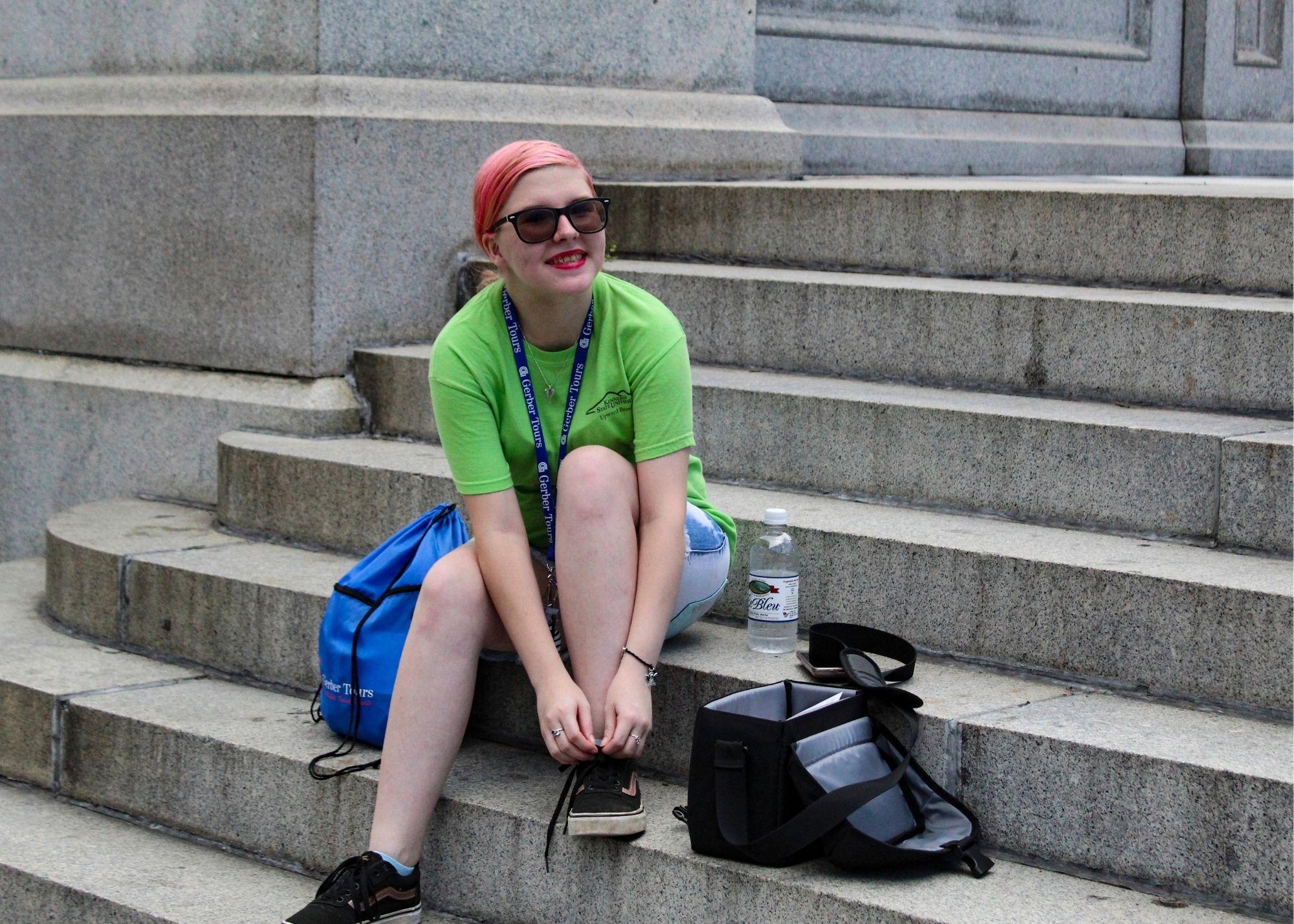 A woman sitting on a set of stairs holding her shoelaces. / KSU TRiO Upward Bound at Rockmart and Cedartown High Schools visit the Atlanta Zoo.
