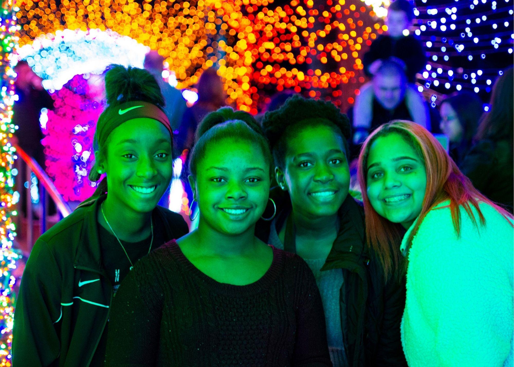 Four students at Atlanta Botanical Gardens with a light display in the background. / KSU TRIO Students have the opportunity to explore and learn about the science behind the Atlanta Botanical Gardens.