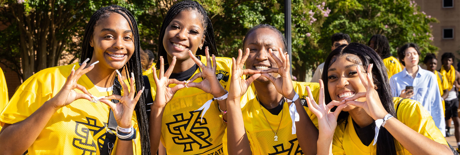KSU students wearing KSU t-shirts giving owl eyes with their hands.