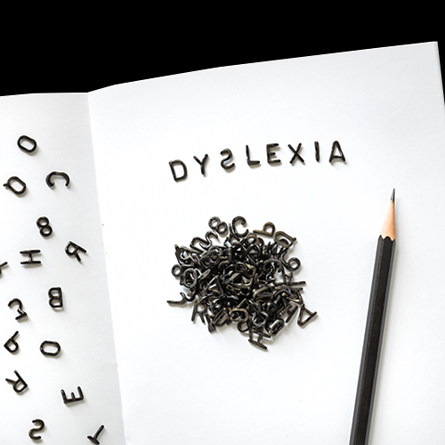 A white notebook with scattered black letters and a pencil, spelling out "DYSLEXIA" at the top, symbolizing the challenges of reading and writing associated with dyslexia.