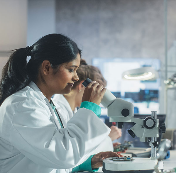 A student in a lab coat peers into a microscope, illustrating hands-on learning in MAT Secondary Science Courses.