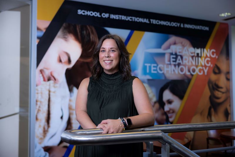 Smiling woman in front of a 'Teaching, Learning, Technology' sign at KSU’s School of Instructional Technology & Innovation.