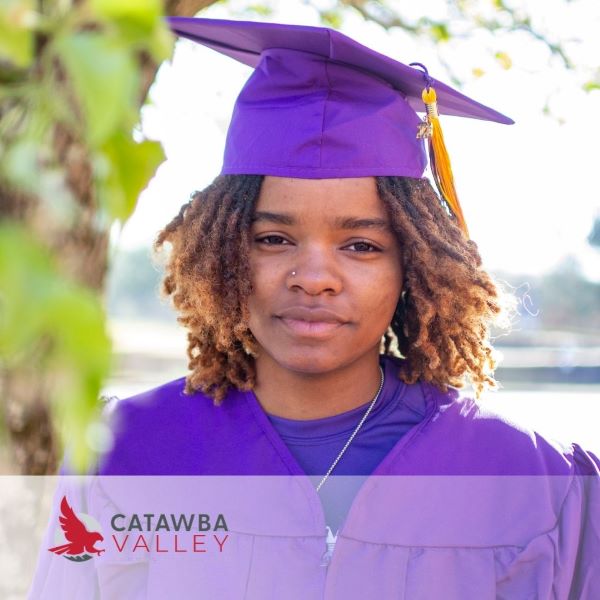 Makiala Bullock, a graduate in a purple cap and gown, in front of a tree with the Catawba Valley logo in the corner.