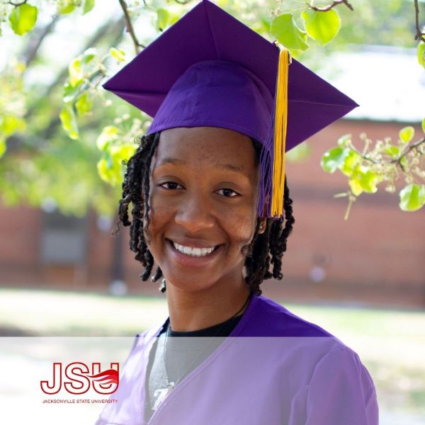 Vially Saint-Louis, a graduate wearing a purple cap and gown with the Jacksonville State University logo in the bottom left corner.