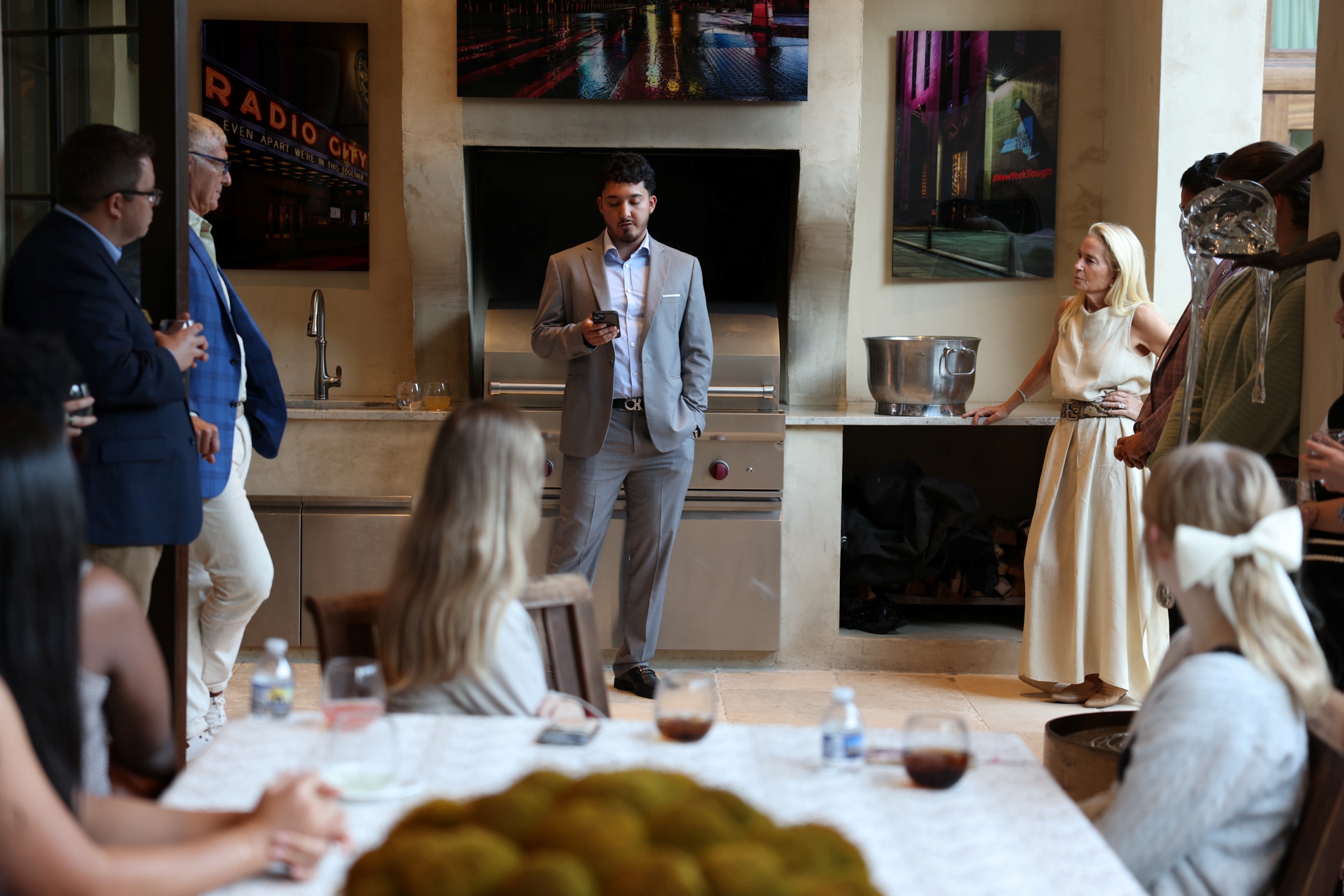 A student dressed in a suit looks at his notes as he delivers remarks in front of a fireplace.