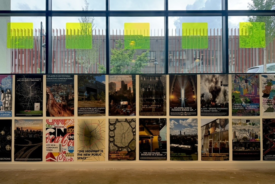 Student-made posters hang on a wall below windows in an industrial setting.