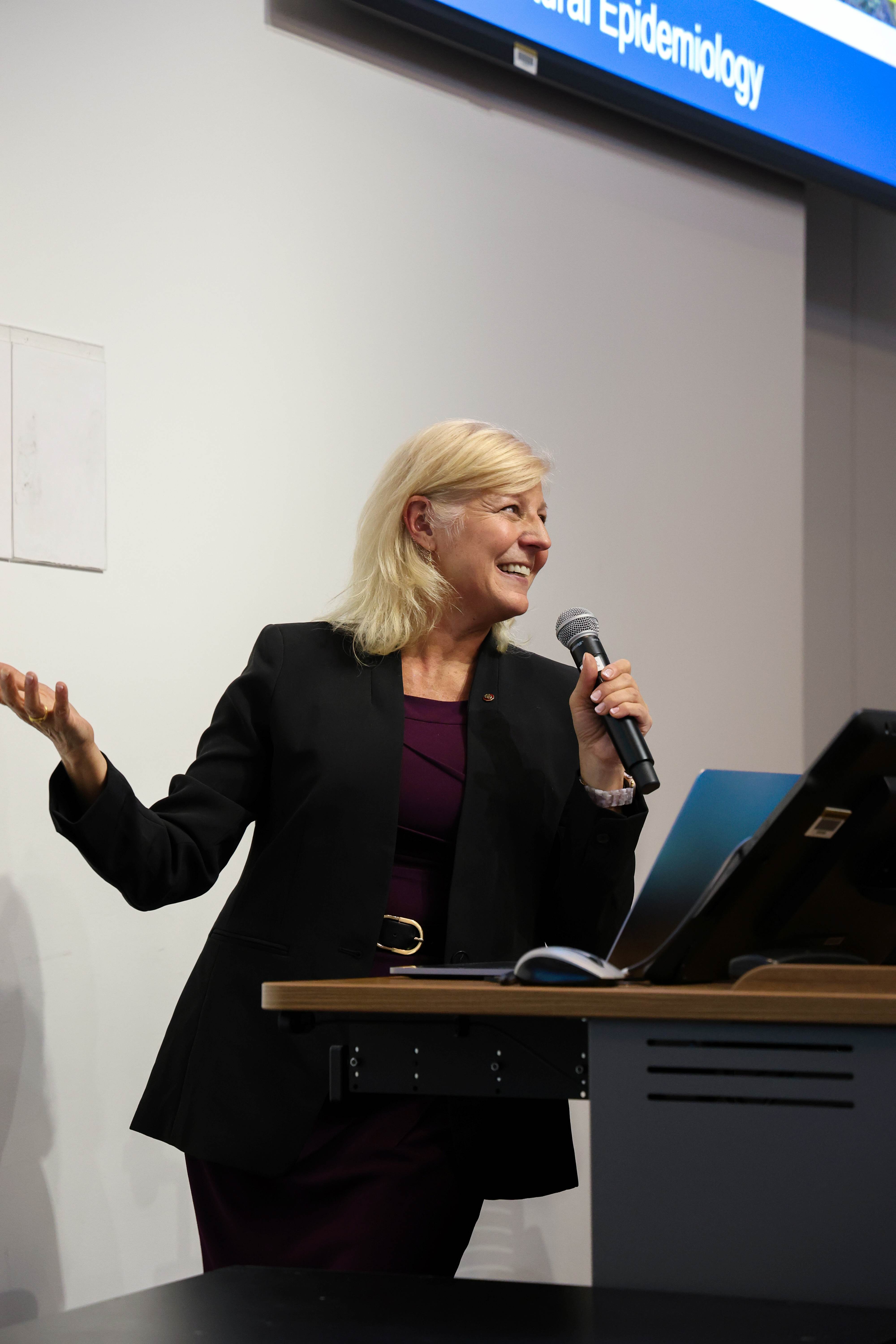 Speaker Liz York smiles as she leans on lecturn holding a microphone.