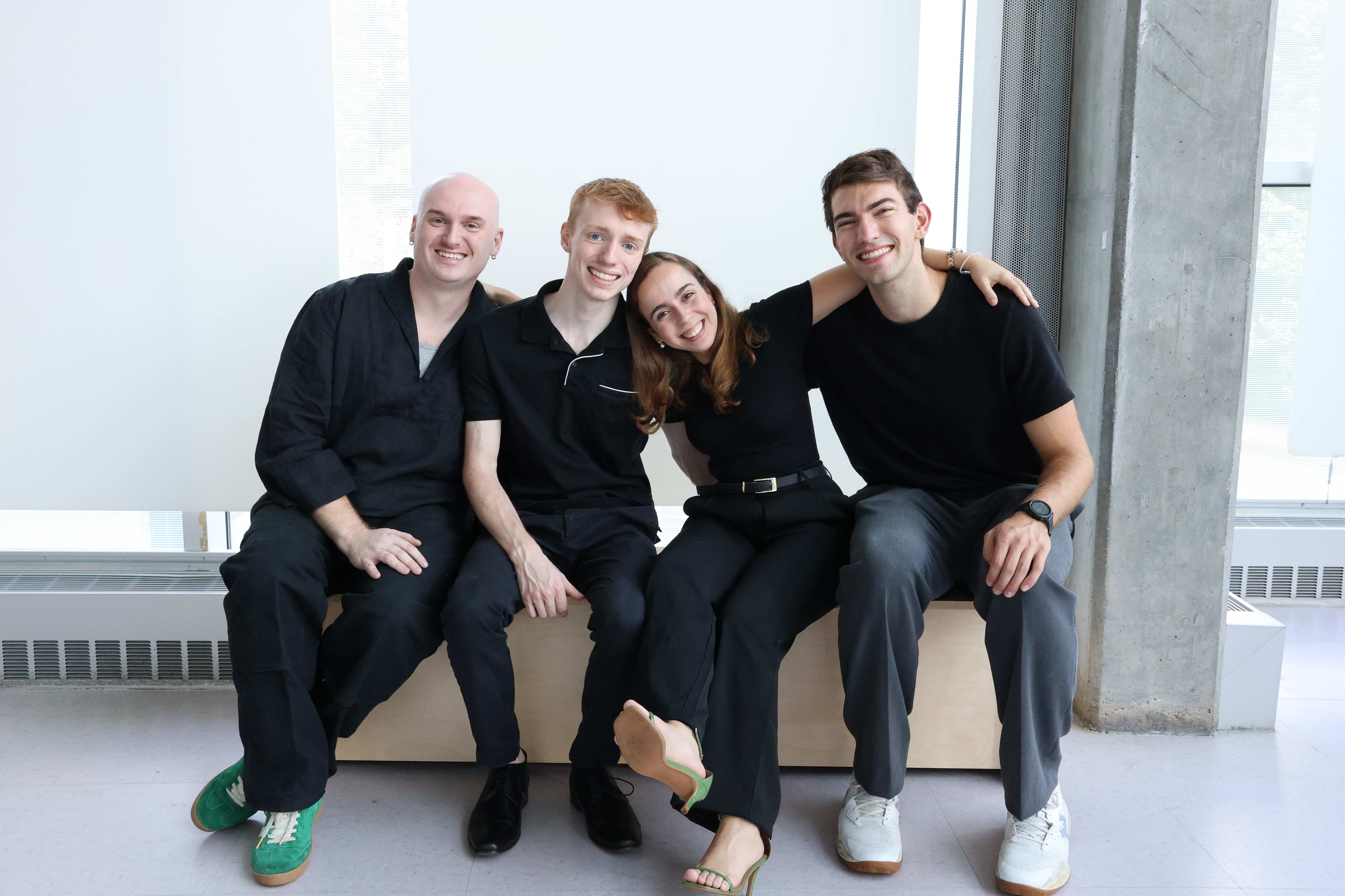 A group of four smiling students seated together on a bench with their arms around one another.