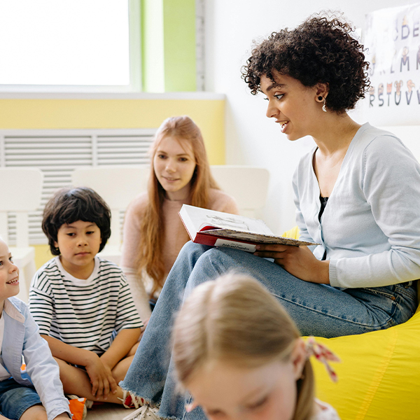 teacher with a book in classroom telling story to little kids