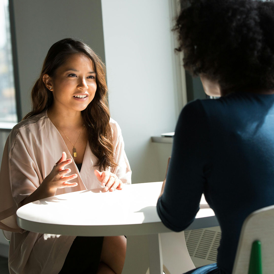 female sitting at desk talking to other employee