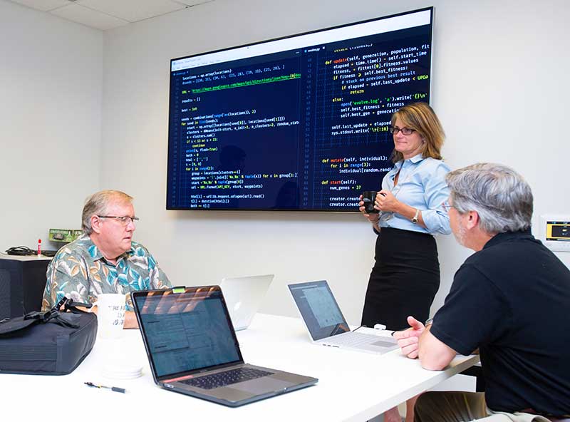 Dr. Priestley working in the lab with students explaining the project code on the monitor behind her.