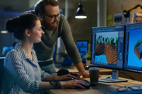 two ksu game development students collaborating at computer with dual monitors