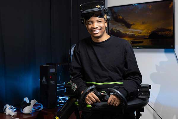 photo of ksu student sitting next to his gaming computer with virtual reality headset propped on head