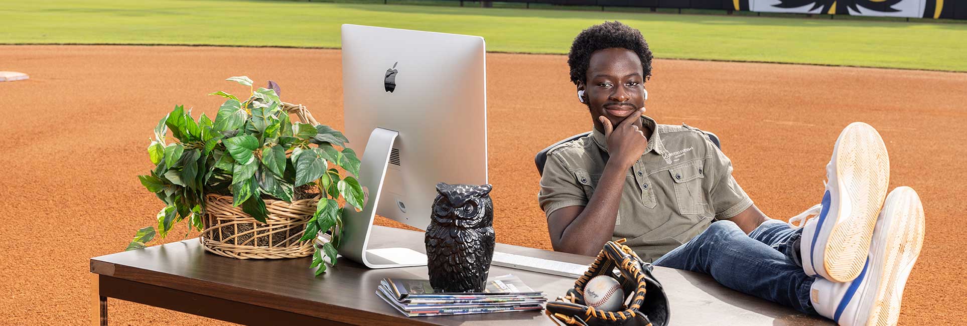 photo of ccse student sitting with his legs up at a desk in the middle of a baseball field