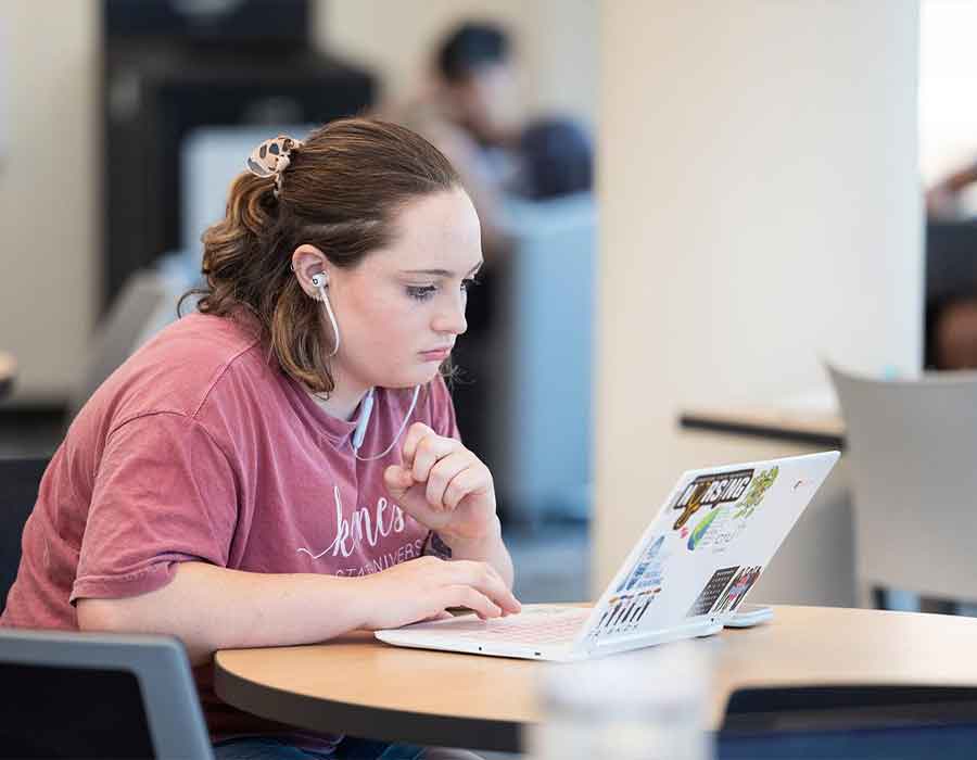 ksu student studying at a table using their laptop.