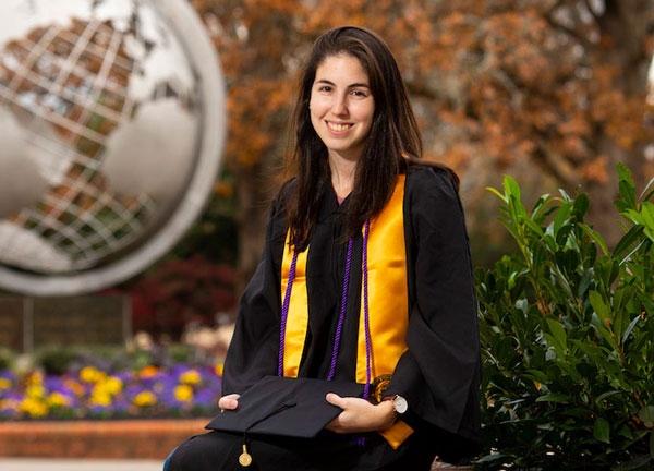 Kim Hertz posing in front of the Globe on the Marietta Campus in graduation apparel.