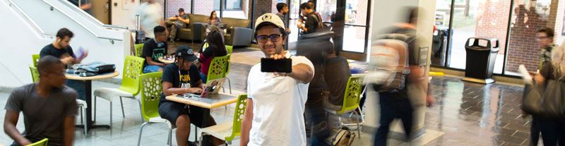 Devan Patel posing with a smart phone as students in the background rush by.