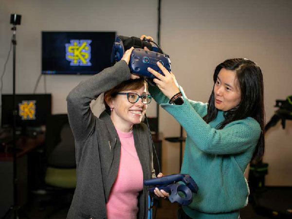 Kennesaw State University Game Design professor Joy Li, right, puts a VR headset on Elena Wood, a professor at Augusta University, as they work on a VR simulation in the VR lab at the Atrium Building. 