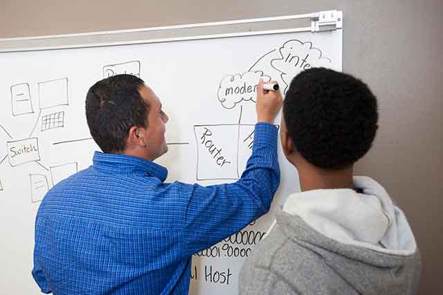 KSU professor writing on white board while student observes.