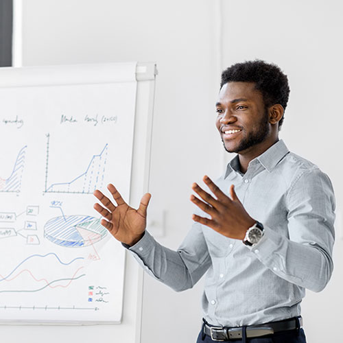 A man presents in front of a whiteboard, gesturing to illustrate his points during a professional presentation.