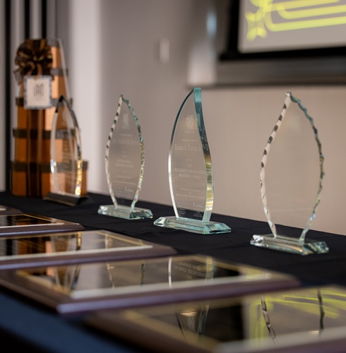 Four glass teardrop awards and for plaques on a black table with five stacked presents in the back corner of the picture.