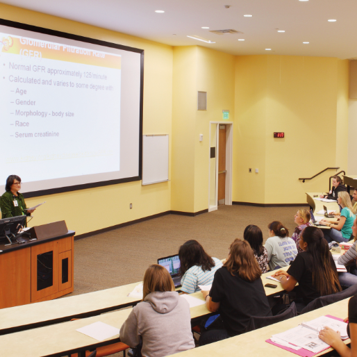 large classroom with teacher at podium speaking to students