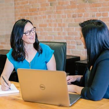 two females smiling in office meeting at desk in front of computer