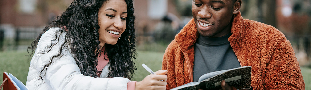 female and male college student sitting outside doing homework on grass