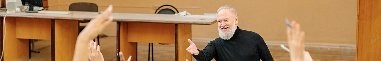 teacher smiling looking at all of his students raising their hand in classroom