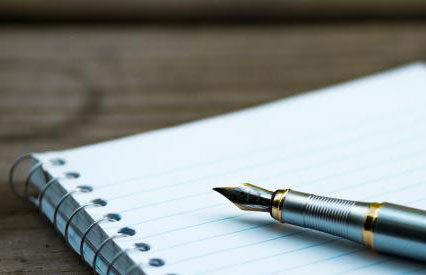 Close-up of a fountain pen resting on a blank, lined spiral notebook, placed on a wooden surface.