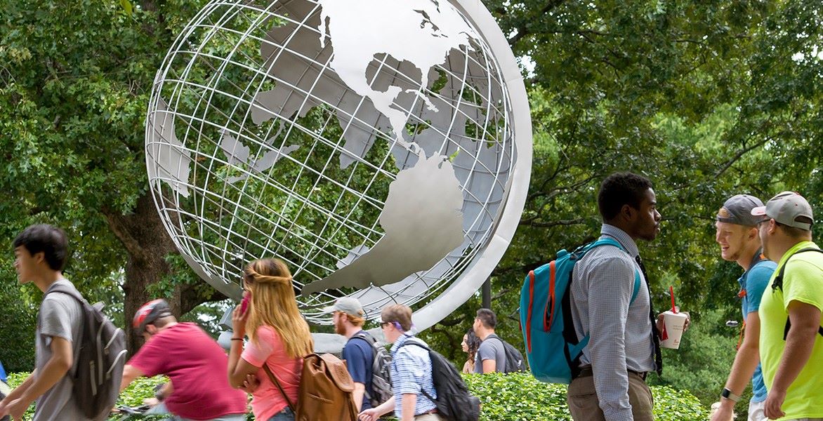 Students walking on campus near a large globe sculpture.