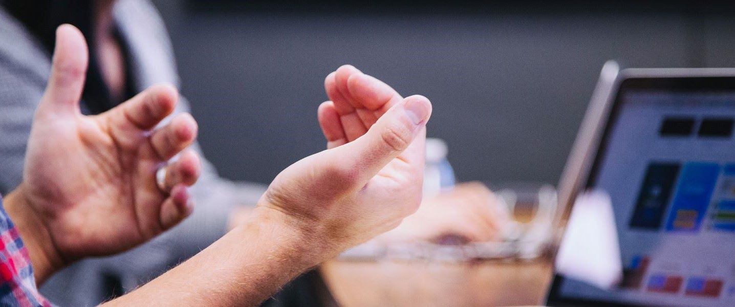 Person gesturing during a meeting with laptop screen visible.