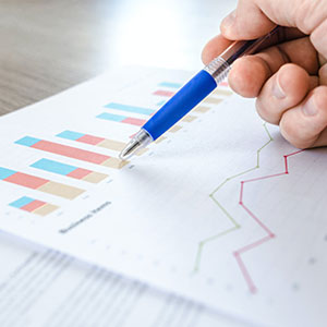 A hand holding a pen over paper displaying a graph, representing research data for the Office of Research New Faculty Resources.