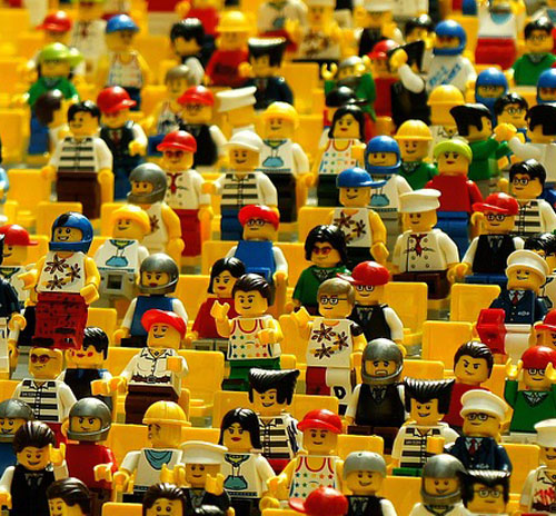 A large group of LEGO figures in a bright yellow classroom, illustrating the impact of environment on student learning.