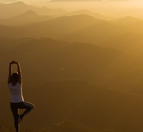 A woman performs yoga on a mountain summit, with breathtaking scenery stretching out in all directions around her.