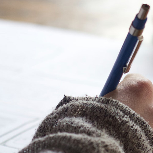 A hand holds a pen, writing on a sheet of paper, indicating a moment of creativity or note-taking.