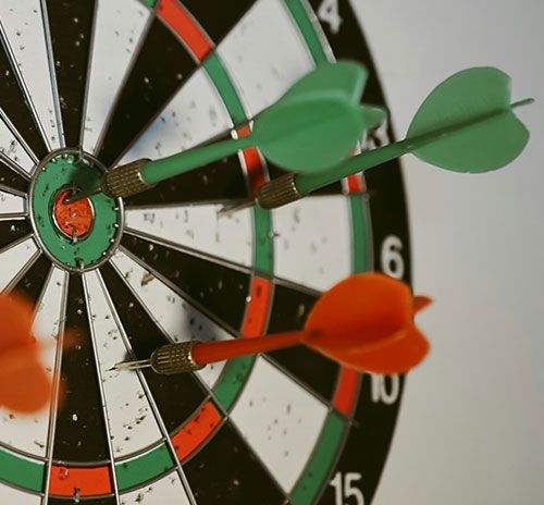 A dart is positioned at the center of a dartboard, symbolizing precision and focus in goal-directed practice.