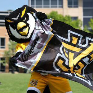 Kennesaw State University mascot enthusiastically waving a university flag on a grassy field, symbolizing school spirit.