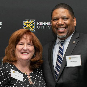A man and woman, both part-time faculty, stand together proudly holding an award.