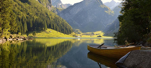 A serene lake with a boat on the shore, framed by majestic mountains in the background.