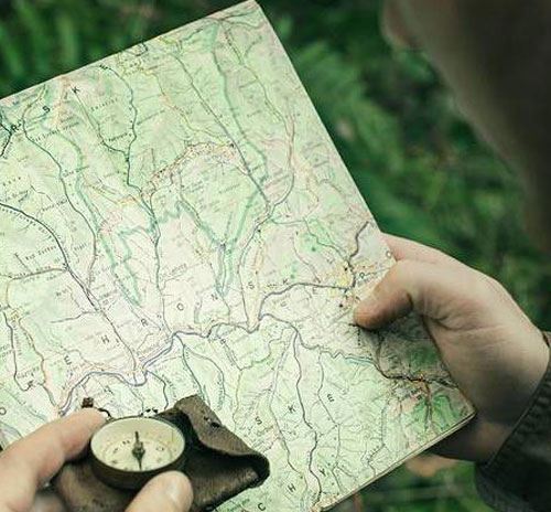 A person in the woods examines a map and compass, symbolizing metacognition in self-directed learning.